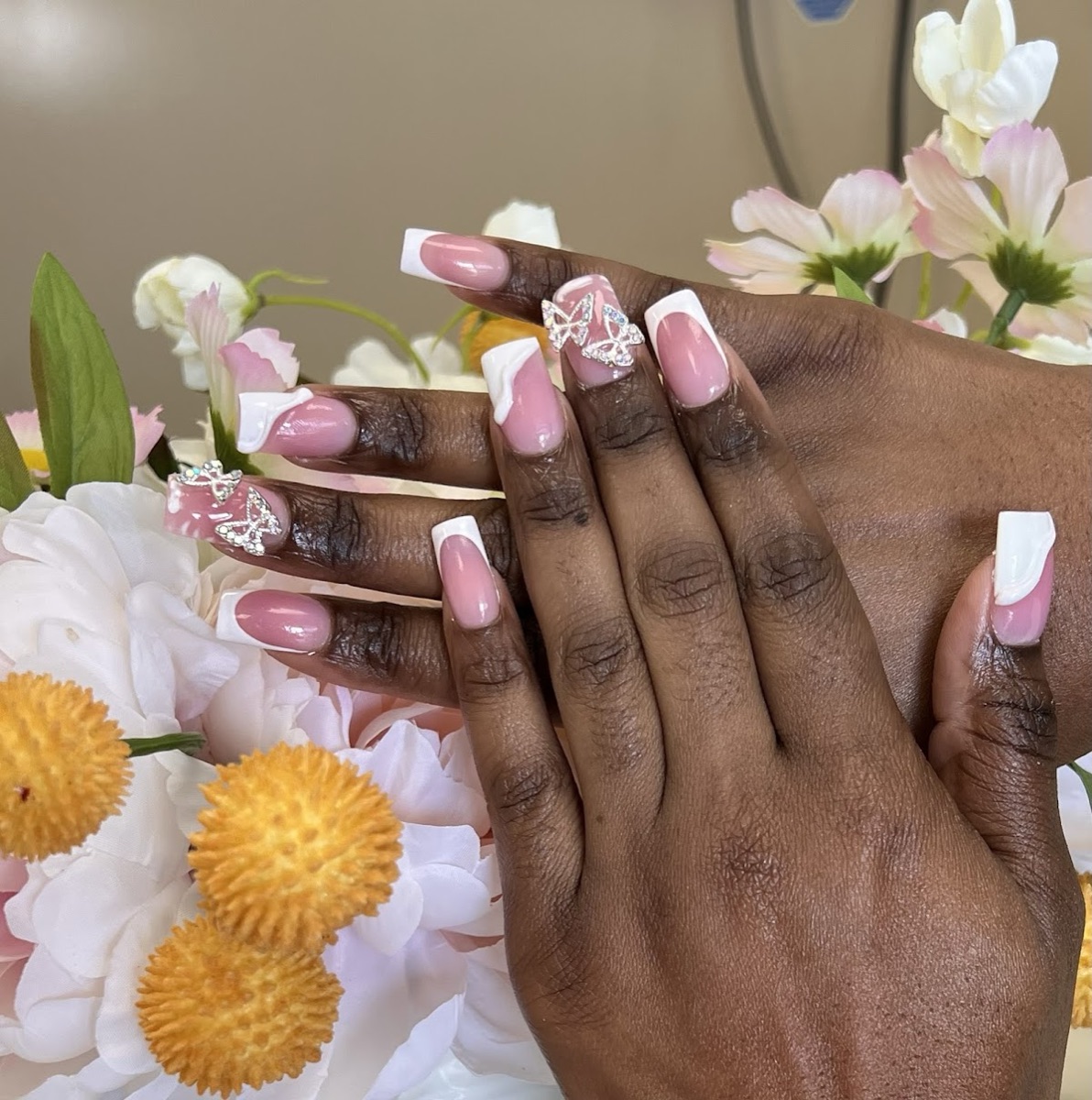 Pink and white French nails with 3D butterfly accents